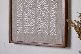 The Samaya Hand Stitched Wall Art - Natural by nkuku features white zigzag embroidery on beige linen, framed in warm brown sustainable mango wood—an elegant accent for your wall décor.