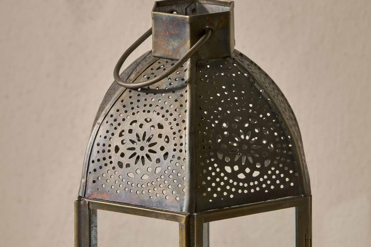 Close-up of nkuku's Sabra Lantern - Aged Antique, featuring a domed top, floral and geometric cut-out patterns, sturdy ring handle, and antique finish—an ideal tealight holder displayed against a plain, light background.
