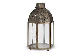 The Sabra Lantern - Aged Antique by nkuku is a hexagonal metal tealight holder with glass panels, a hinged door, latch, domed top with cut-out patterns, round handle, ball feet, and an antique finish for vintage charm.