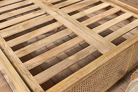 A close-up of a wooden coffee table with a slatted top and rattan panels that mirror the artisanal style of nkuku's Saharsa Cane & Mango Wood Bed. The natural wood grain pops, set against a matching wood floor.