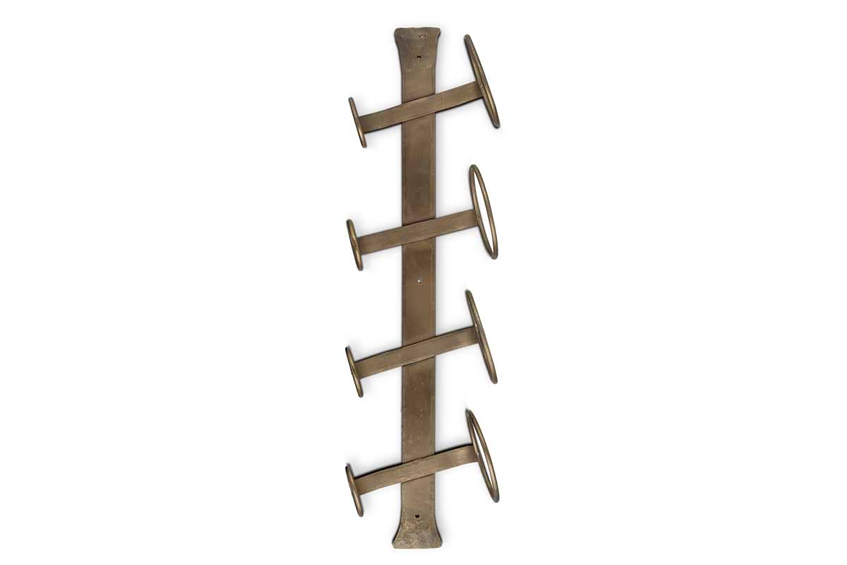 The nkuku Shray Iron Wine Rack in Antique Brass is a wall-mounted holder with four angled arms, alternating left and right, and rings at the end of each right-facing arm.