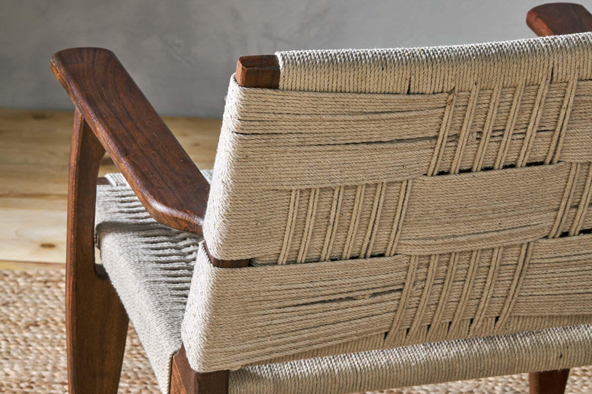 Close-up of the Surat Woven Lounger by nkuku, showcasing a hand-woven natural cotton rope back and seat with dark wood armrests and frame for timeless appeal.