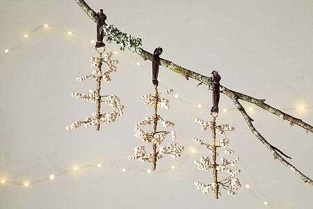 The nkuku Tanu Mango Wood Beaded Baubles - Brass & Natural (Set of 3) feature gold and natural beaded ornaments, each hanging from a dark ribbon—perfect as unique Christmas tree decorations or festive table decor.