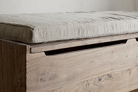 A close-up of the nkuku Teni Reclaimed Wood Storage Bench in a natural finish, featuring an upholstered linen cushion in light grey and a recessed handle for easy lid opening.