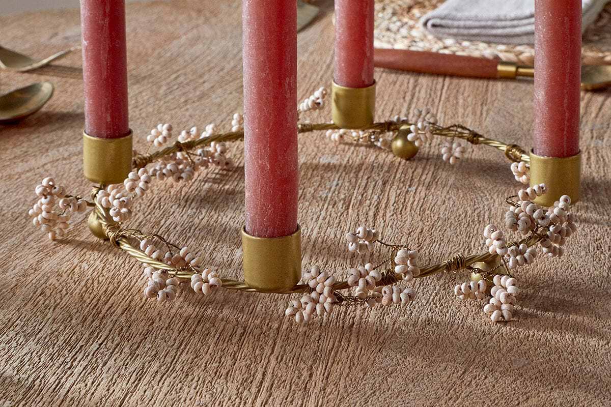 The nkuku Tanu Mango Wood Beaded Candle Holder in brass and natural features four red candles with delicate white berry clusters, creating an elegant, rustic centerpiece ideal for festive tablescapes.