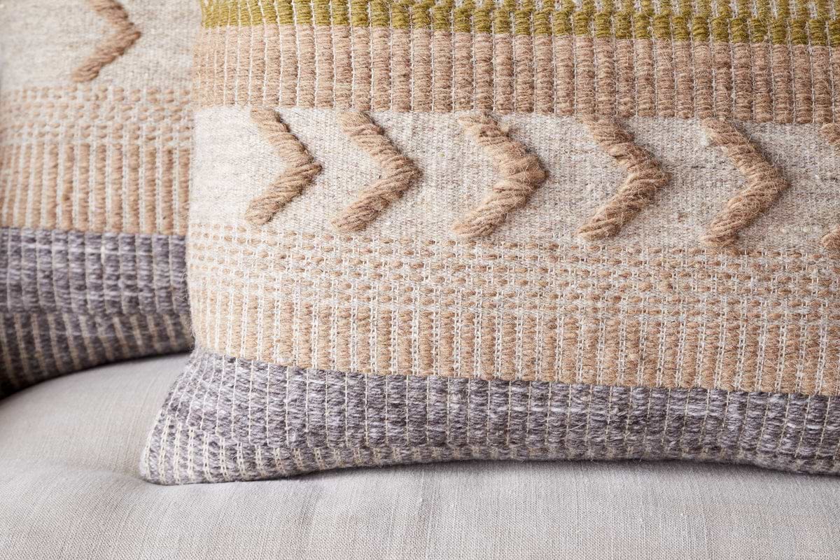 The Tuleeka Wool Cushion Cover - Ochre by nkuku features a textured woven design with geometric patterns in beige, gray, ochre, and olive green on a light background. Raised arrow shapes and stripes add depth to this decorative pillow.