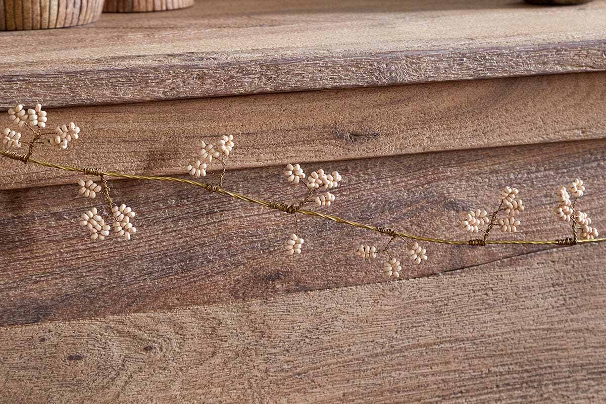 The Tanu Mango Wood Beaded Garland by nkuku features natural wood beads and brass accents, elegantly draped on a surface to showcase its delicate craftsmanship and warm, earthy tones.