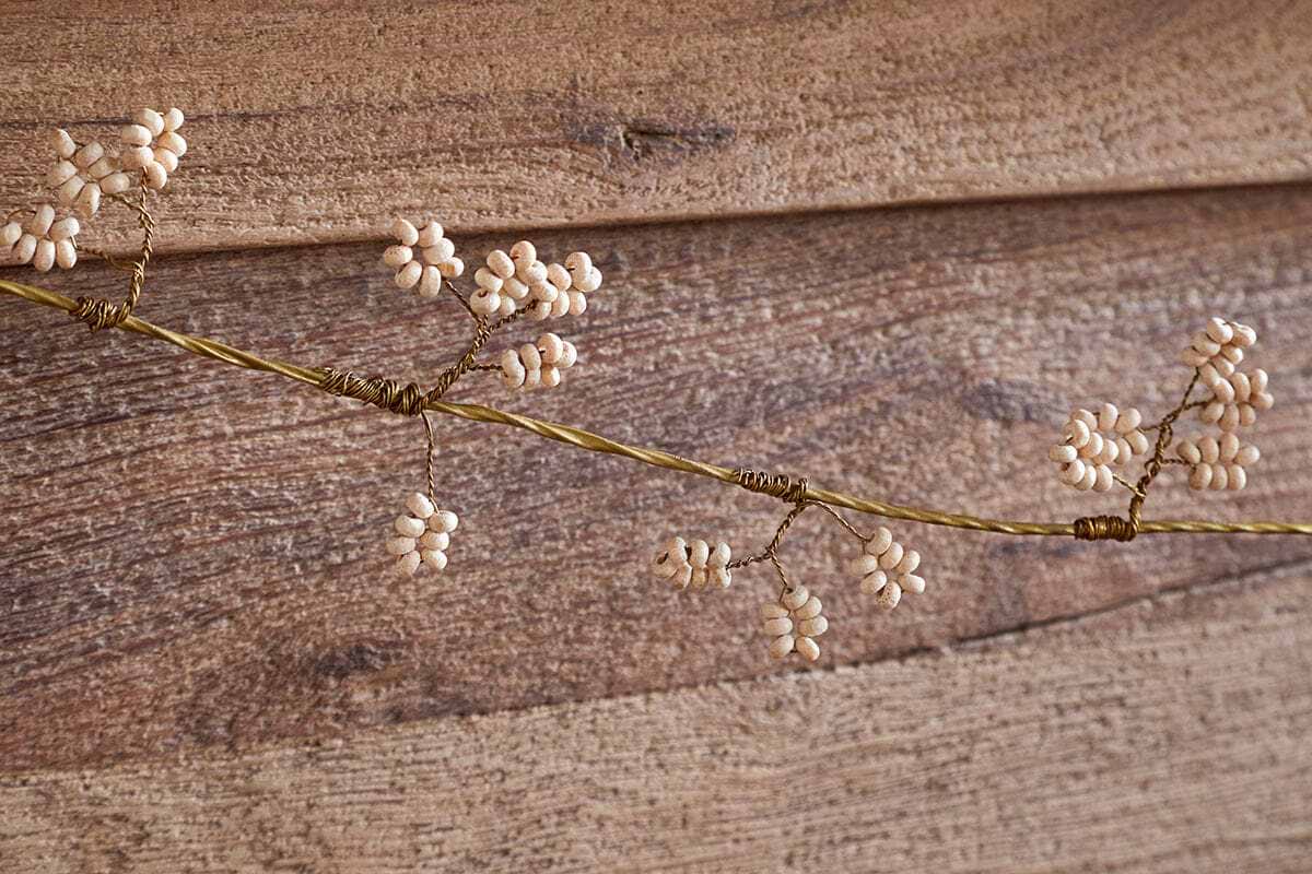 The nkuku Tanu Mango Wood Beaded Garland features natural and brass beads strung along a delicate wire, resembling festive clusters. Displayed on rustic wooden planks, it adds an elegant, handcrafted touch to your decor.