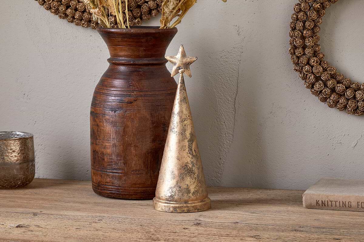 The Talna Tree Bell - Antique Brass by nkuku, a gold cone-shaped piece reminiscent of an antique brass bell, sits beside a vase.