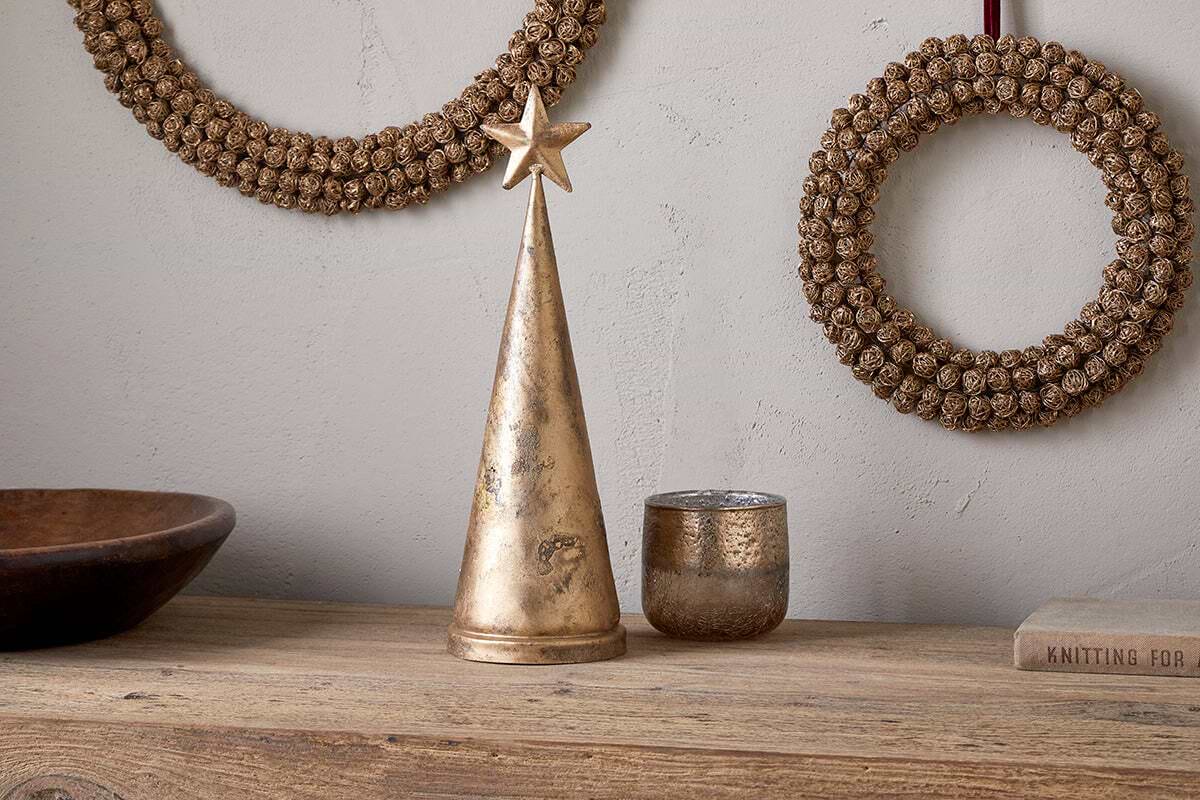 The nkuku Talna Tree Bell in antique brass sits on a wood shelf, making a perfect festive ornament or a stylish addition to your Christmas decor.