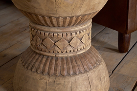 Close-up of the Taru Carved Side Table - Natural by nkuku, featuring a hand-carved leg with intricate diamond and vertical line patterns inspired by Indian design, set on a wooden floor.