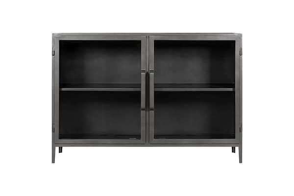 The Takua Iron Sideboard by nkuku features a black metal frame, two glass front doors with slim vertical handles, and four slender legs. Inside, a central shelf divides the storage space. Its minimalist style draws on strong industrial design influences.