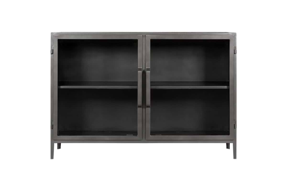 The Takua Iron Sideboard by nkuku features a black metal frame, two glass front doors with slim vertical handles, and four slender legs. Inside, a central shelf divides the storage space. Its minimalist style draws on strong industrial design influences.