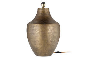 The nkuku Tanda Etched Statement Table Lamp in Antique Brass (Extra Large) features a textured, metallic gold vase-like base with a narrow neck and black socket. An electrical cord with switch extends from its base against a plain white background.