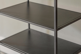 Close-up of the Tanvi Display Shelf by nkuku in black—a minimalist, narrow unit with three dark shelves and slim vertical supports against a light wall. Its matte surfaces are smooth, perfect for modern display.