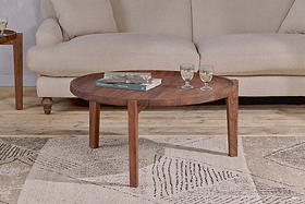 The nkuku Umar Mango Wood Coffee Table - Dark Brown, with its sculptural circular design, displays two glasses and books on a textured rug in front of a cream-colored sofa.