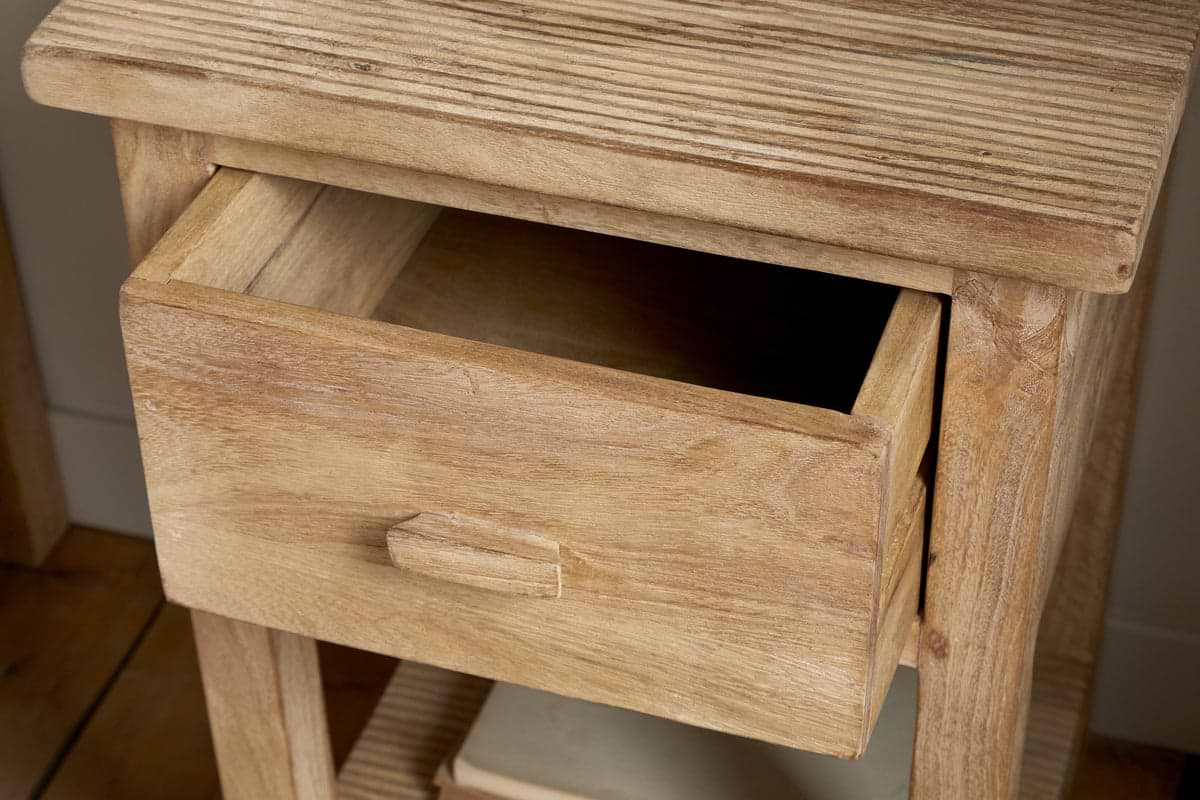 A close-up of the nkuku Vivan Grooved Bedside Table - Natural, showing its slim design, single partially open drawer with a simple rectangular handle, and visible natural wood grain.
