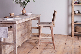The nkuku Vinay Woven Counter Chair - Natural pairs perfectly with a rustic mango wood kitchen island featuring shelves and a towel hook, offering functional charm and style for your space.