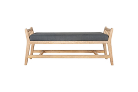 The Avanthi Upholstered Sleigh Bench by nkuku features a simple, modern design with angled legs, vertical slat sides, an elegant carved frame in natural wood finish, and a charcoal gray upholstered cushion seat.