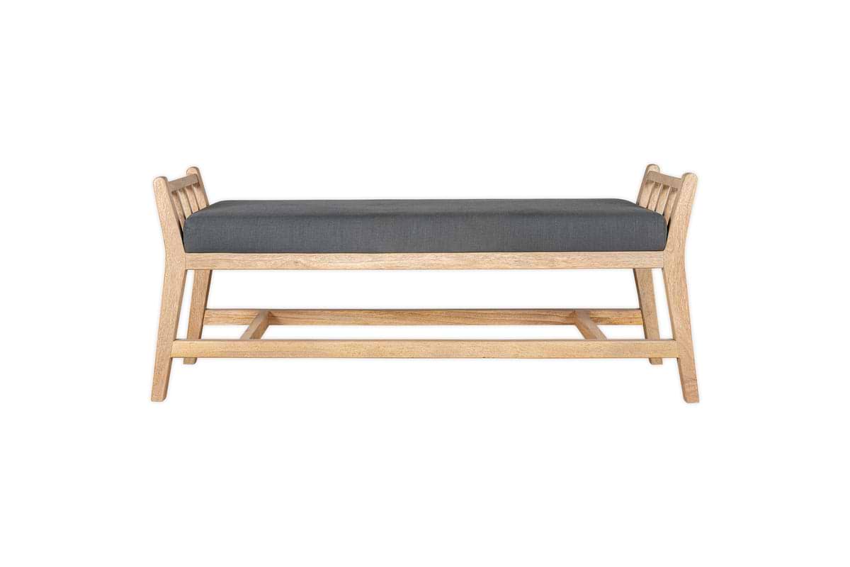 The Avanthi Upholstered Sleigh Bench by nkuku features a simple, modern design with angled legs, vertical slat sides, an elegant carved frame in natural wood finish, and a charcoal gray upholstered cushion seat.