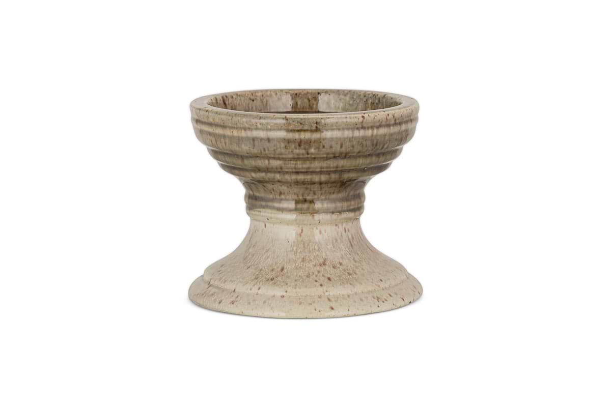 The Cabra Reactive Glaze Candle Holder by nkuku features a wide bowl, ribbed detail, and flared base. Its olive and natural reactive glaze offers a rustic look. The candle holder is centered on a plain white background.