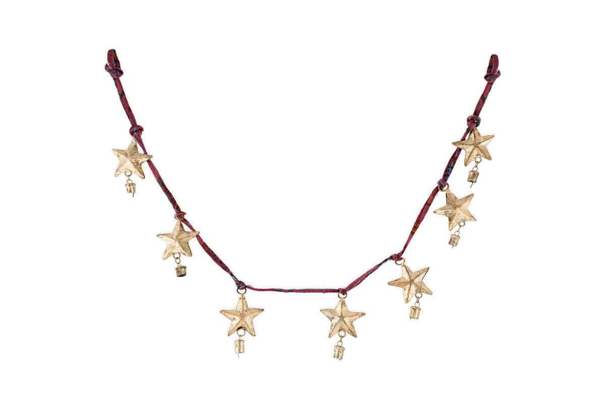 The Didi Star Garland - Antique Brass by nkuku features seven handcrafted brass stars with gold charms on a dark red cord, combining rustic and celestial details for a festive, Christmas-inspired look.