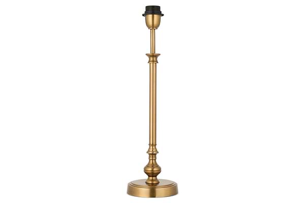 The Ehadi Antique Table Lamp by nkuku features a tall, slender antique brass base with decorative detailing and a round pedestal, shown without shade or bulb, set against a white background.