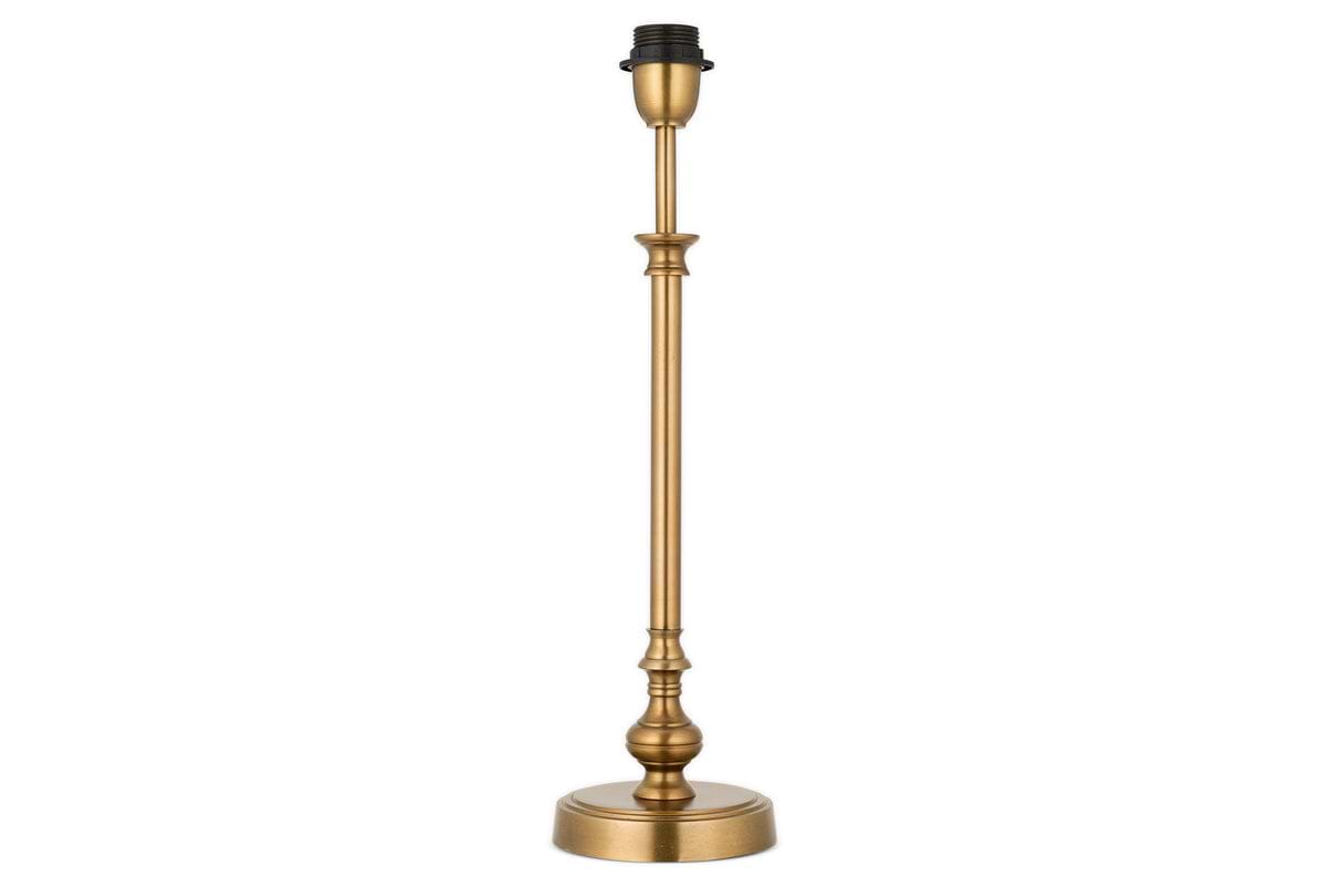 The Ehadi Antique Table Lamp by nkuku features a tall, slender antique brass base with decorative detailing and a round pedestal, shown without shade or bulb, set against a white background.
