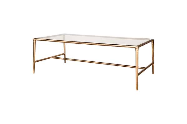 The nkuku Gilasi Cast Metal & Glass Coffee Table in Antique Brass features a rectangular glass top, a slender metal frame with four straight legs, and a minimal design, shown against a plain white background.