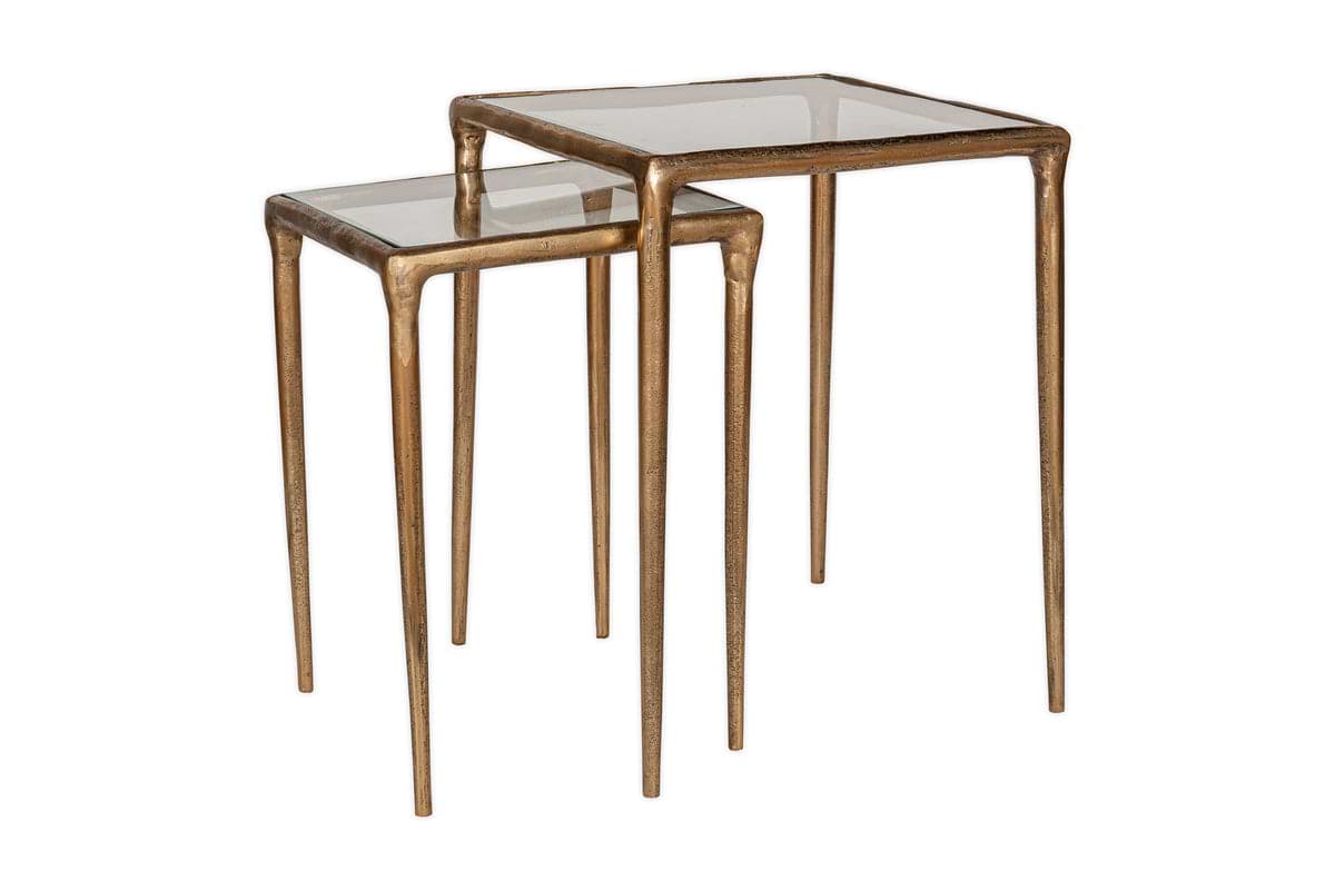 The nkuku Gilasi Cast Metal & Glass Nesting Side Tables (Set of 2) feature slim antique brass frames and clear square glass tops in two heights, designed to partially nest for versatile styling.
