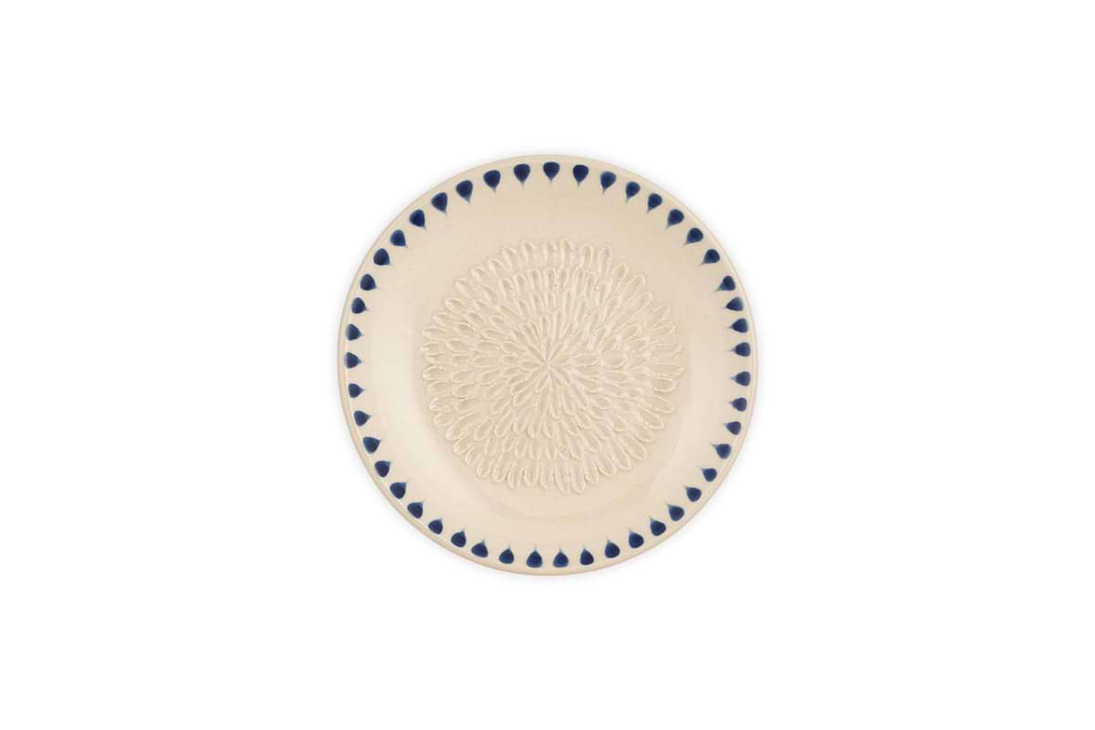 The nkuku Indigo Drop Garlic Grater in cream and indigo features an intricate raised looped center pattern and a border of blue teardrop shapes, with a subtle hand-painted design from the Indigo Drop collection.