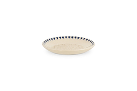 The nkuku Indigo Drop Garlic Grater in Cream & Indigo is a shallow, round beige ceramic plate with a textured center and hand-painted dark blue triangle accents around the rim, perfect for grating garlic.