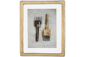 The Jahala Wall Hung Photo Frame in Antique Brass by nkuku displays a photo of two rustic, vintage wooden hair picks on a gray surface, with Beautifully Handmade and Home & Lifestyle overlaid on the image.