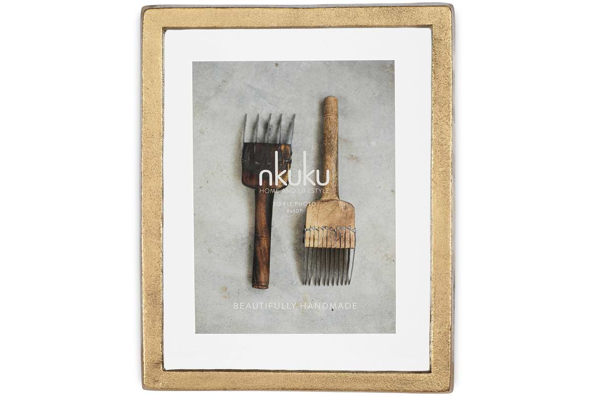 The Jahala Wall Hung Photo Frame in Antique Brass by nkuku displays a photo of two rustic, vintage wooden hair picks on a gray surface, with Beautifully Handmade and Home & Lifestyle overlaid on the image.