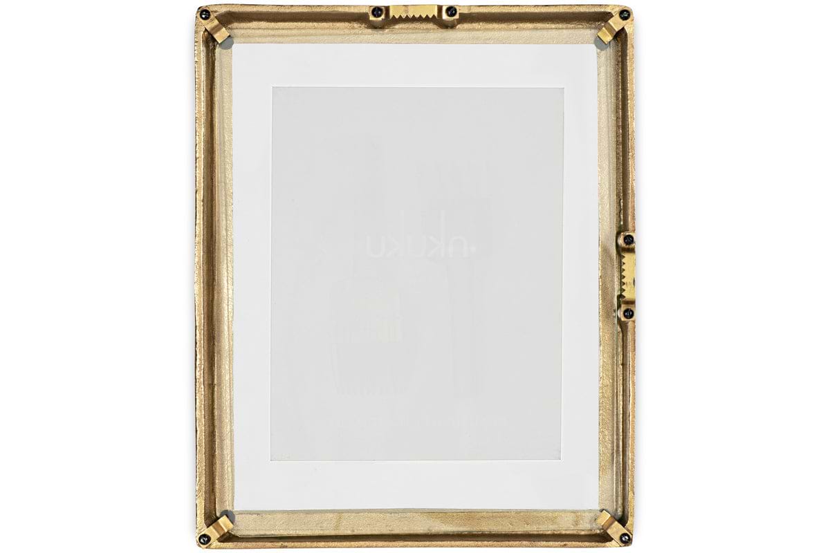 The Jahala Wall Hung Photo Frame by nkuku features a rectangular antique brass frame with decorative ridges and black screws at the corners and sides, and includes a white mat. Shown empty against a white background.