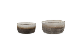 The nkuku Janka Tealight Holders - Smoked Charcoal (Set of 2) feature round, frosted glass with rough, uneven edges—perfect for adding rustic charm as tealight holders or decorative accents in any setting.