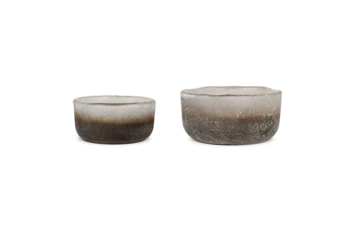 The nkuku Janka Tealight Holders - Smoked Charcoal (Set of 2) feature round, frosted glass with rough, uneven edges—perfect for adding rustic charm as tealight holders or decorative accents in any setting.