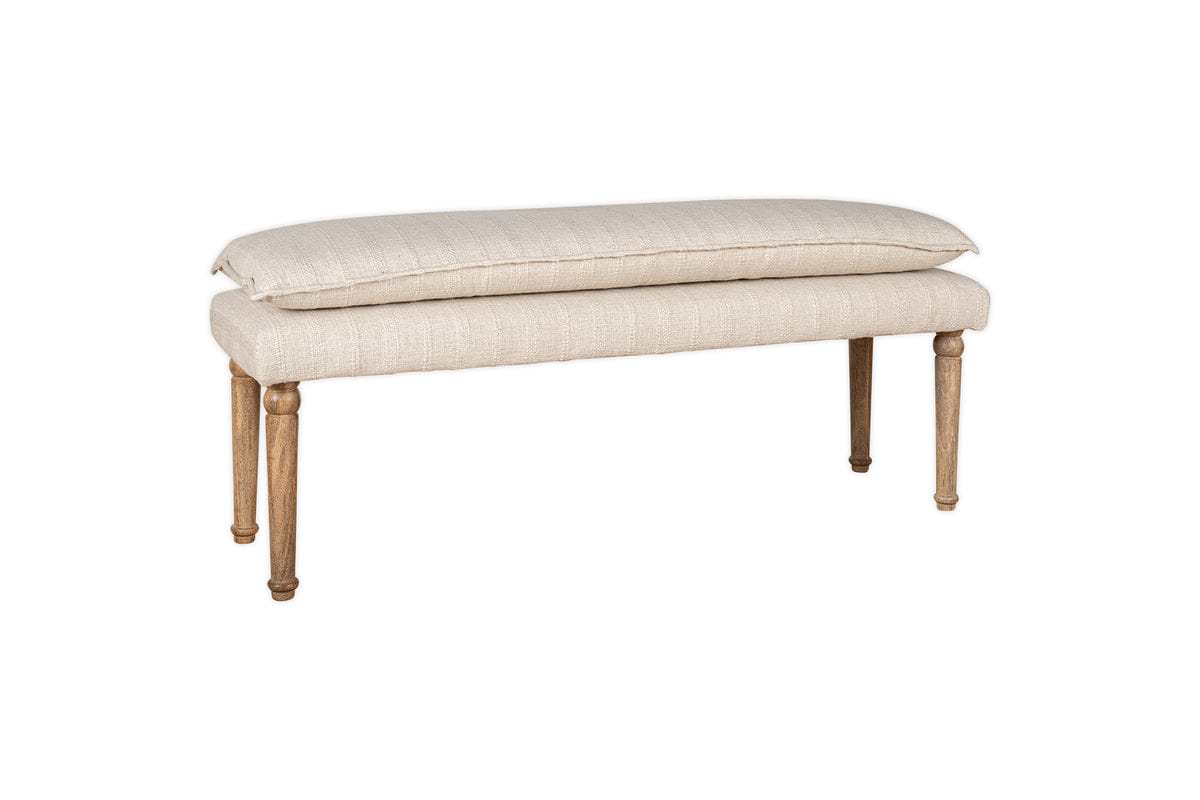 The nkuku Kiana Cotton Upholstered Bench in natural features a thick cushioned seat and four light wooden legs, making it an elegant accent piece displayed against a white background.