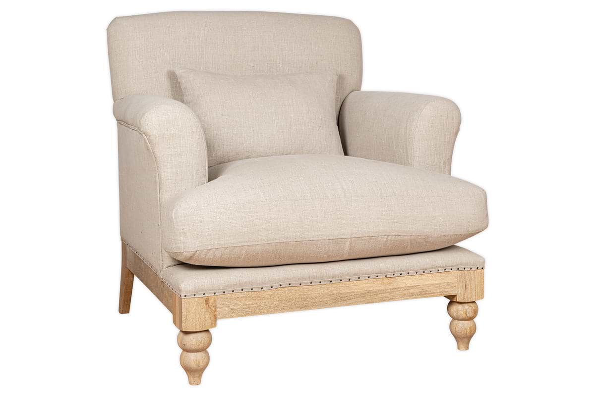 The Kashi Linen Armchair - Natural by nkuku features beige upholstery in natural linen, rounded arms, a plush seat cushion, matching lumbar pillow, and exposed light mango wood legs with decorative carvings.