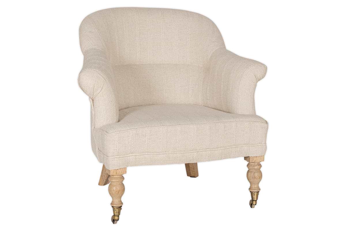 The Kiana Cotton Armchair - Natural by nkuku features beige cotton upholstery, a curved backrest, rounded arms, and hand-carved mango wood legs—two with brass caster wheels.