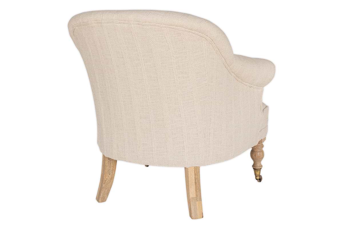 The Kiana Cotton Armchair - Natural by nkuku is shown from the back at an angle on a white background. This beige cotton upholstered chair features hand-carved mango wood legs, with one front leg finished with a brass caster wheel.