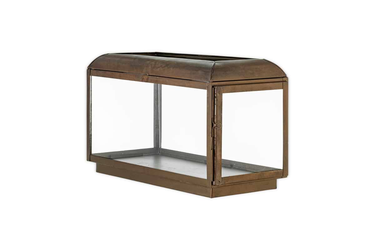 The nkuku Kiwanda Wide Lantern in Antique Brass features a rectangular glass and metal design with a hinged side door and flat base, echoing antique lantern charm, displayed against a plain white background.