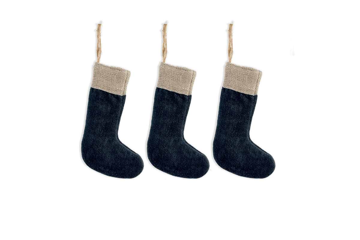 The nkuku Karru Cotton Velvet Mini Stockings - Indigo (Set of 3) feature indigo velvet bodies with beige, textured cuffs, hanging in a row on white strings against a plain backdrop to highlight their minimalist, rustic style.