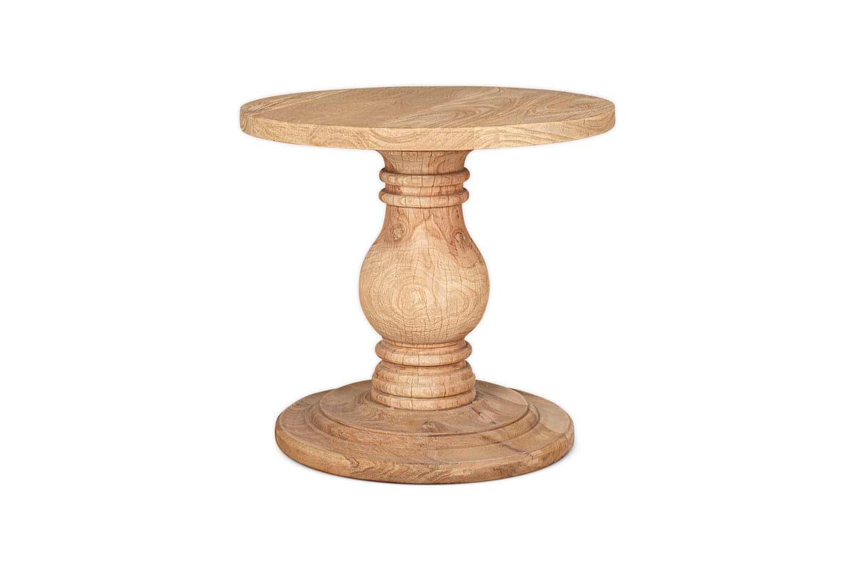 The nkuku Laya Round Carved Side Table in a natural wood finish features a sculptural, thick pedestal base and showcases its elegant grain, photographed against a white background.