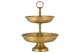 The Mahika Stand - Antique Brass by nkuku is a two-tiered gold metal stand with textured bowls and a top handle, ideal as a centrepiece for festive tablescapes or for displaying fruits, desserts, or snacks.