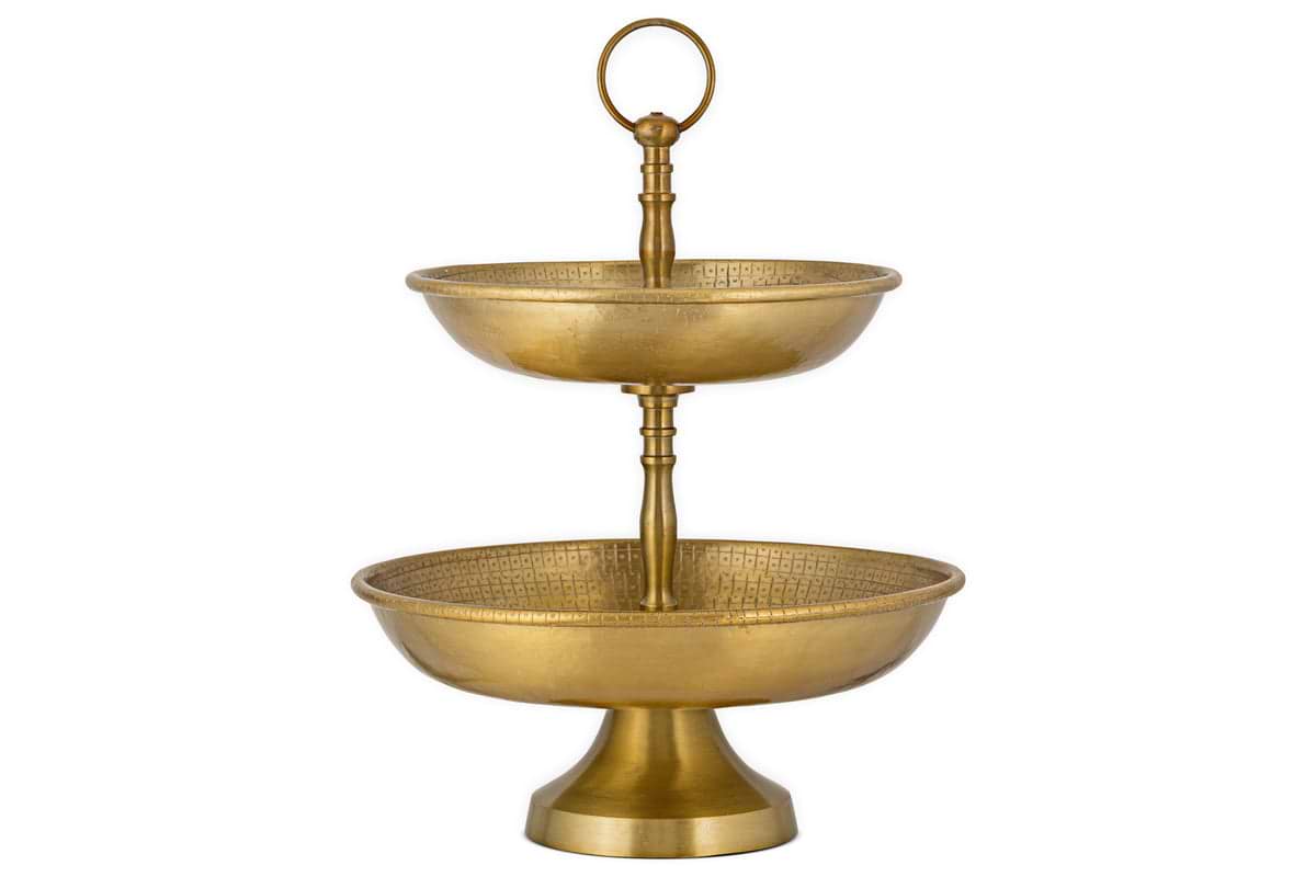 The Mahika Stand - Antique Brass by nkuku is a two-tiered gold metal stand with textured bowls and a top handle, ideal as a centrepiece for festive tablescapes or for displaying fruits, desserts, or snacks.