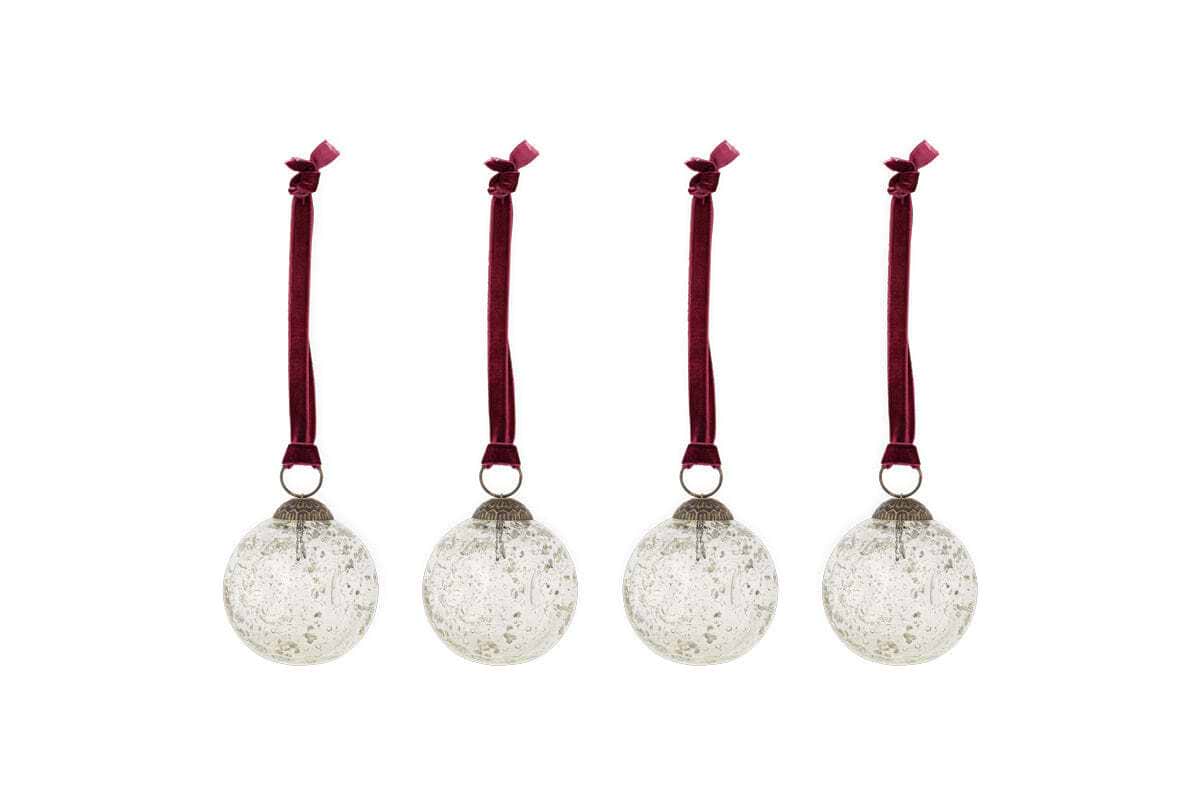 The nkuku Nishan Pinched Baubles - Clear (Set of 4) feature round, recycled glass ornaments with silver caps and burgundy velvet bows, offering a speckled, vintage look that’s perfect for festive decor.