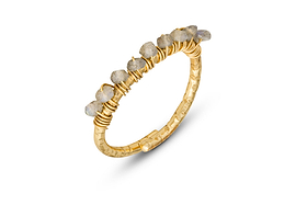 The Vani Labradorite Ring by nkuku features a thin gold-plated band with a textured finish, topped with wire wrap and a row of pale gray labradorite stones, casting a soft shadow on a white background.