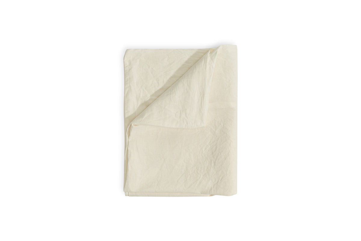 The Cela Hemp & Cotton Duvet Cover - Natural by nkuku is neatly folded against a white background, with one corner turned up to showcase its soft, lightweight blend and subtle texture—ideal for sustainable bedding.
