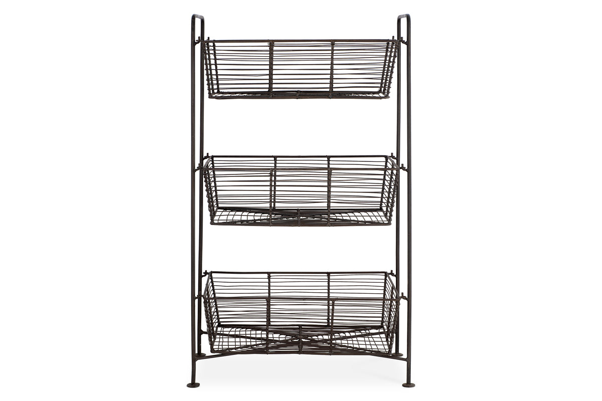 The nkuku Inkollu Three Tier Storage Stand in antiqued brass has rectangular open-wire baskets stacked vertically on a minimalist frame with four slender legs, ideal for kitchen organization and storage.